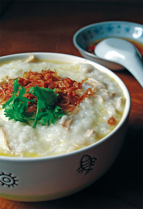 A bowl of chicken congee with egg, fried shallot, and Chinese parsley.