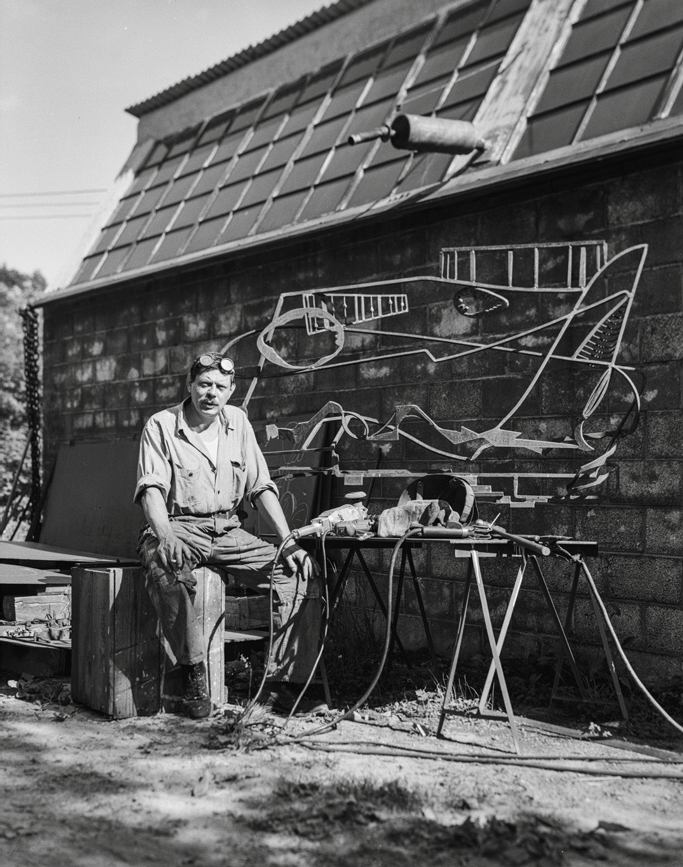 David Smith with Hudson River Landscape, 1951, photographed outside his workshop at Bolton Landing, New York, c. 1951. Photo: The Estate of David Smith, New York. © 2022 The Estate of David Smith / Licensed by VAGA at Artists Rights Society (ARS), NY.